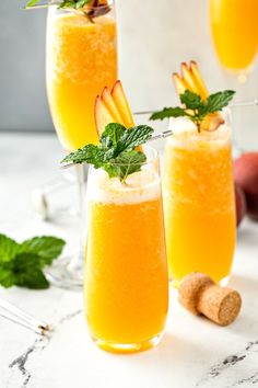 two glasses filled with orange juice and garnished with mint, on a marble surface