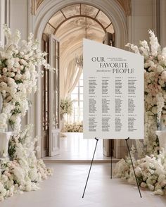 a large white sign sitting in the middle of a room filled with flowers and greenery