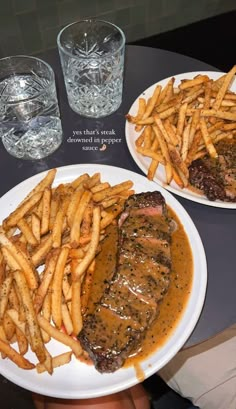 two plates with steak, fries and gravy on them next to water glasses