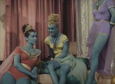 two women in costumes are sitting on a couch and one woman is looking at the camera