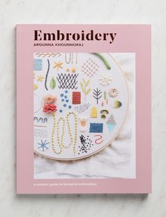 the cover of embroidery book on a white table with pink trimming and an embroidered design