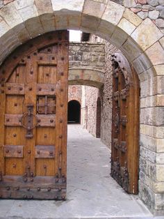 two wooden doors are open in an old brick building with stone walls and arched doorways