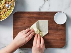 a woman is wiping up her napkin on a cutting board next to a bowl of food