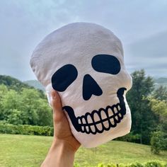 a person holding up a skull pillow in front of a field with trees and bushes