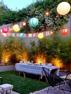 an outdoor dining area with paper lanterns strung from the ceiling and table set for dinner