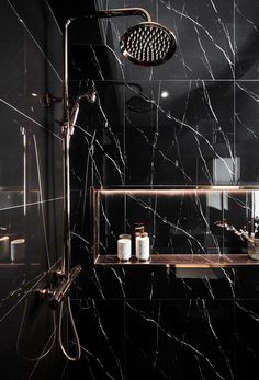 a bathroom with black marble walls and flooring, shower head, and hand held faucet