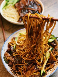 the noodles are being lifted by chopsticks over the plate with meat and vegetables