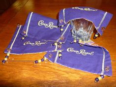 three purple towels with gold beaded trim and glass cup on them sitting on a wooden table