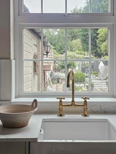 a white kitchen sink sitting under a window next to a bowl on top of a counter