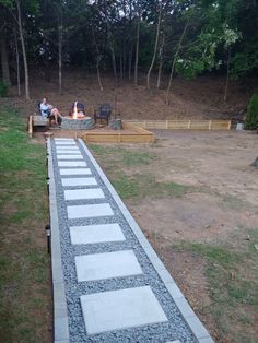 two people sitting at a fire pit in the middle of a yard with stone walkway