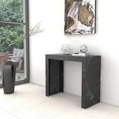 a black marble console table in front of a large window with a painting on the wall