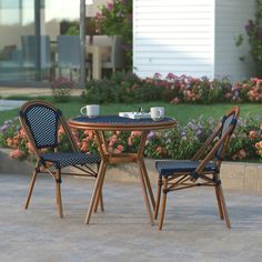 two chairs sitting at a table with cups on it in front of some flowers and bushes