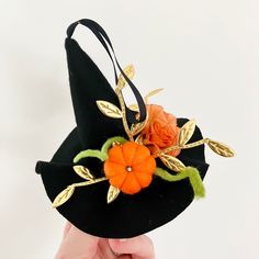 a hand holding a black hat with orange flowers on the front and green leaves on the back