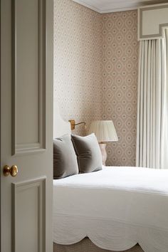 a white bed sitting under a window next to a lamp on top of a table