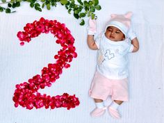 a baby is laying next to some flowers and the number two on it's side