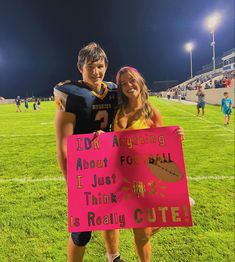 two people standing on a football field holding a pink sign that says i do not arguing about football it just think this is really cute