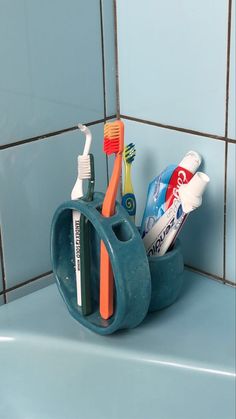 toothbrushes and toothpaste in a cup on a blue tiled countertop