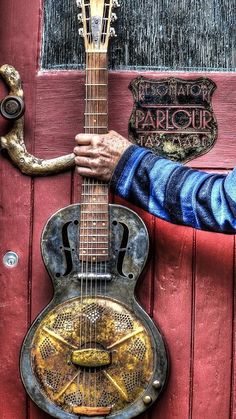 a man is holding an old guitar in front of a red door with the word parlor on it