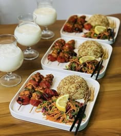 three trays filled with different types of food on top of a wooden table next to glasses of milk