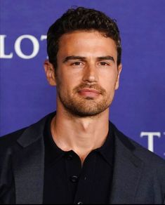 a close up of a person wearing a suit and black shirt with a blue background