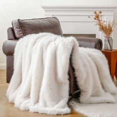 a living room with a couch and chair covered in a white fluffy blanket next to a fireplace