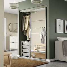 an open closet with clothes hanging on the wall and drawers in front of it, next to a bed