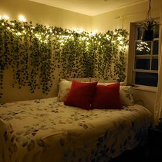 a bed with two red pillows on top of it next to a plant covered wall