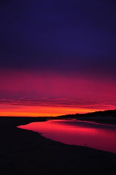 the sun is setting at the beach with purple and red colors in the sky over water