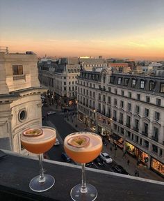 two cocktails are sitting on the ledge of a building overlooking a cityscape