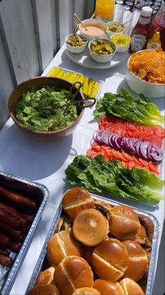 hot dogs and salads are laid out on a long table with bowls of condiments