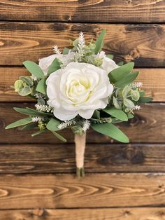 a bridal bouquet with white flowers and greenery on a wooden background in front of wood planks