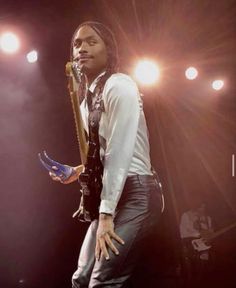 a man with dreadlocks standing on stage holding a guitar in his right hand