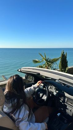 a woman driving a car down a road next to the ocean