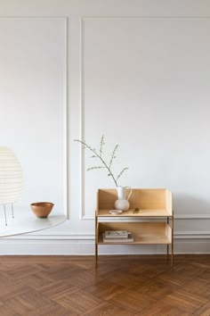 a white vase sitting on top of a table next to a wooden shelf with a plant in it