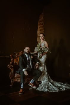 a bride and groom posing for a photo in their wedding day attire, sitting on an old chair