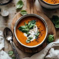 two bowls of tomato soup with basil leaves and sour cream on the top one bowl is filled with cheese