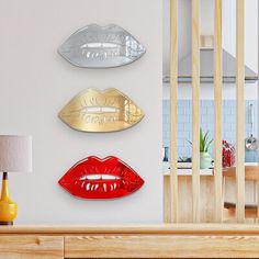 three metal lips are hanging on the wall next to a table with a lamp and vase