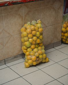 a bag full of oranges sitting on the floor next to a tiled counter top