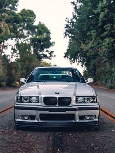 a silver car parked on the side of a road next to some trees and bushes