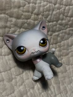 a small white cat figurine sitting on top of a bed next to a pillow