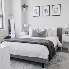 a bedroom with white walls and gray bedding, framed pictures on the wall above the bed