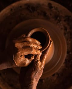 a person's hands holding a clay pot on a potter's wheel in the dark