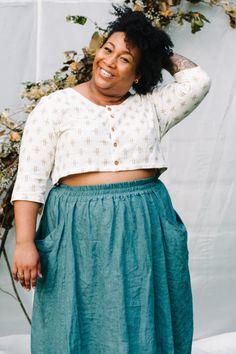 a woman standing in front of a white backdrop wearing a blue skirt and crop top