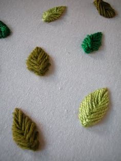 four different types of leaves on a white table cloth with green thread and yellow thread