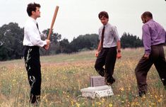 three men are standing in a field holding baseball bats and an ice chest with a cooler underneath them