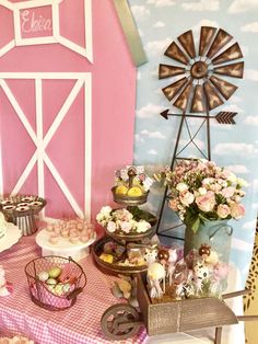 a table topped with lots of desserts next to a pink barn and blue wall