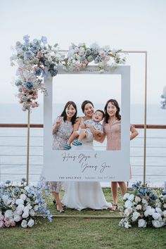 three women standing in front of a photo frame with flowers and greenery on it