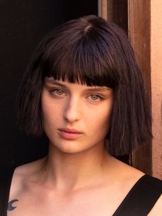 a close up of a person wearing a black dress and hair with bangs on her head