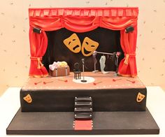 a cake that is shaped like a theater stage with two masks on the curtain and music instruments in front of it