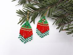 the beaded christmas tree earrings are hanging from a pine branch with green and red beads